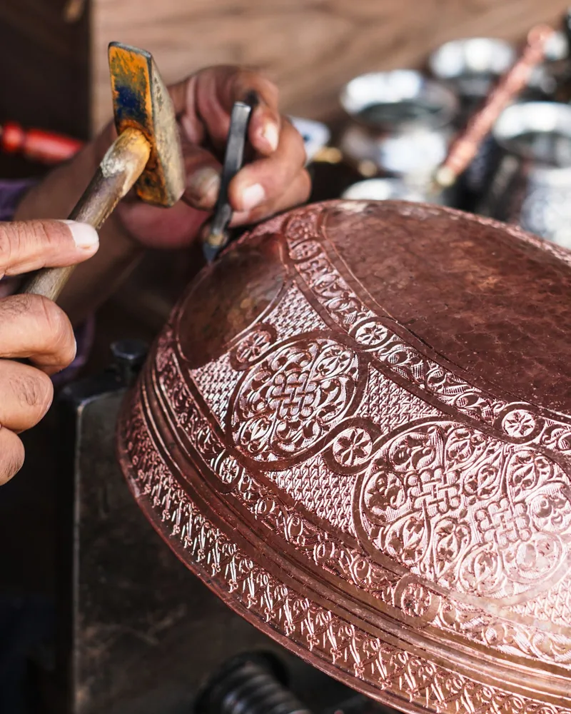Detalle de un cuenco de cobre con ornamento cincelado, con el fondo matizado a puntos y el cincel apoyado sobre la superficie curva.